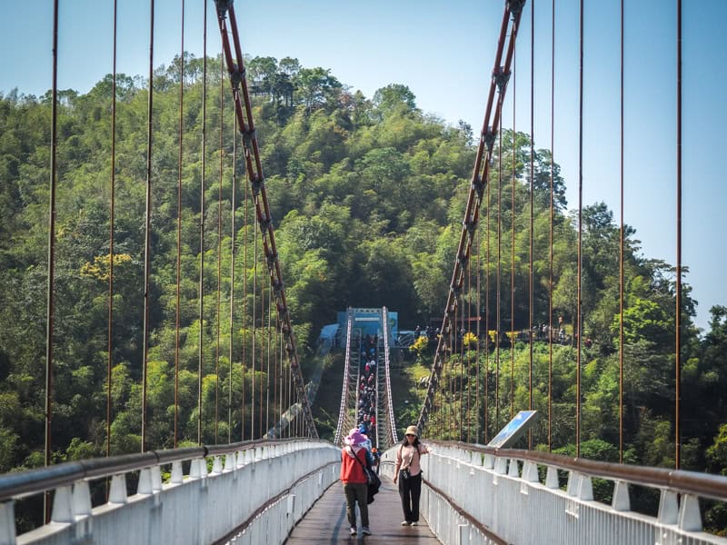 Looking down Taiping Suspension Bridge, with two elderly walking away from the camera and a tour group of people at the far end