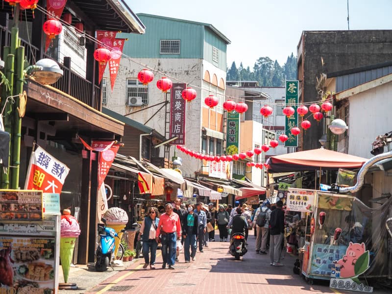 Some pedestrians walking down some old shopfronts on either side of Taiping Old Street, with strings of red lanterns hanging above