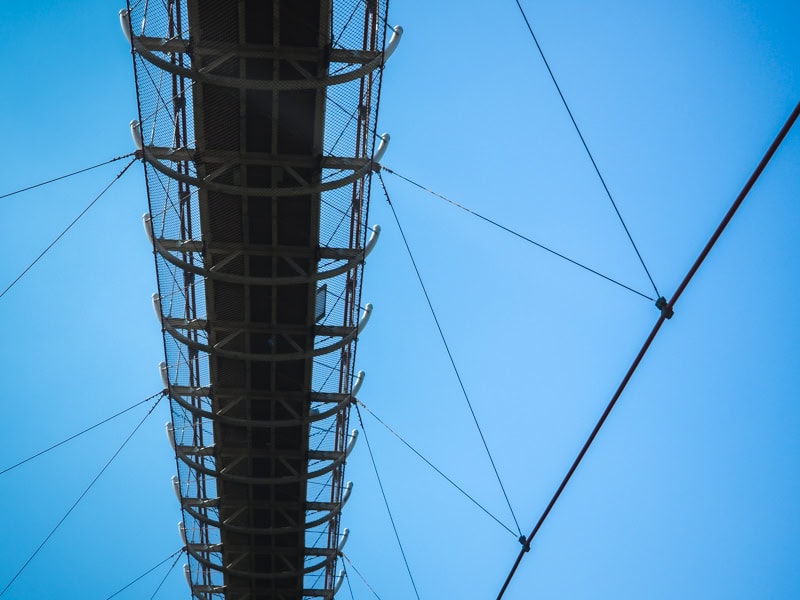 Looking up at a suspension bride and its support cables with a blue sky above