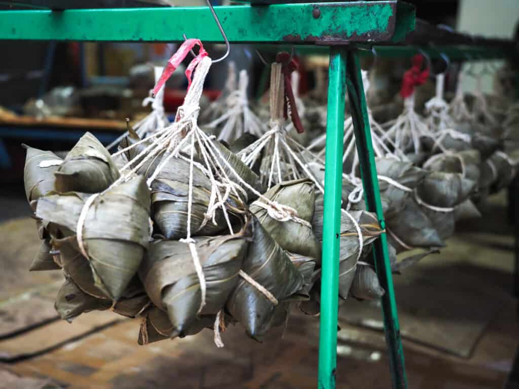 Several bunches of zongzi hanging on white strings from a green rack