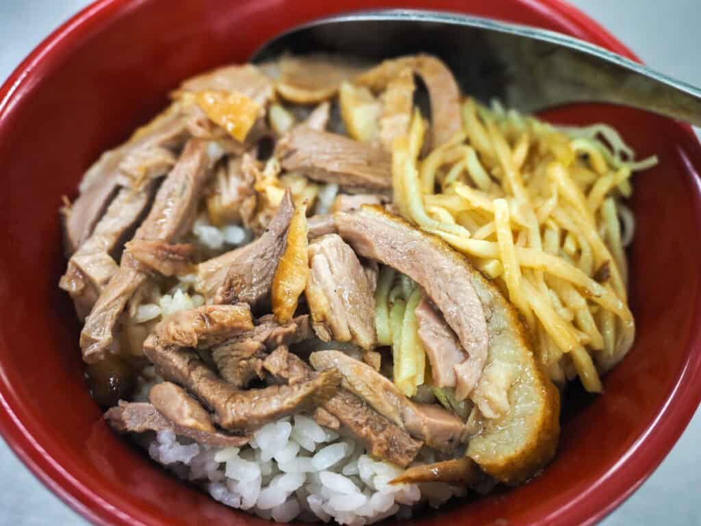 Close-up of a small red bowl of rice with duck meat and bamboo slices
