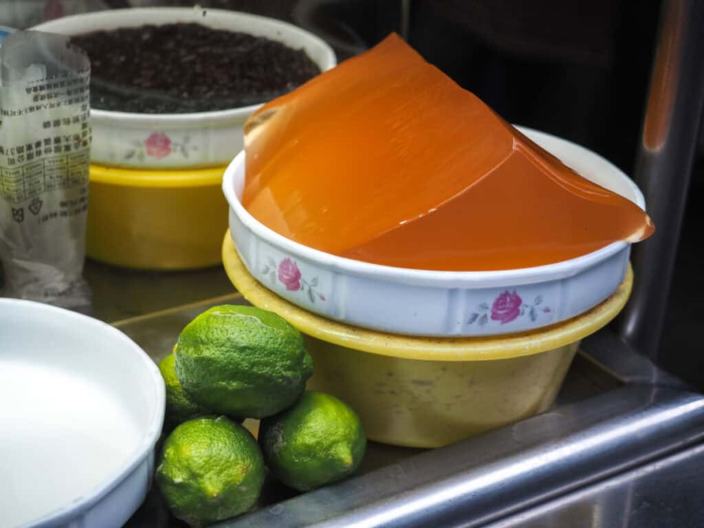 Close up of a large chunk of aiyu jelly in a bowl next to some green lemons on a stall on Sanmin Street Market