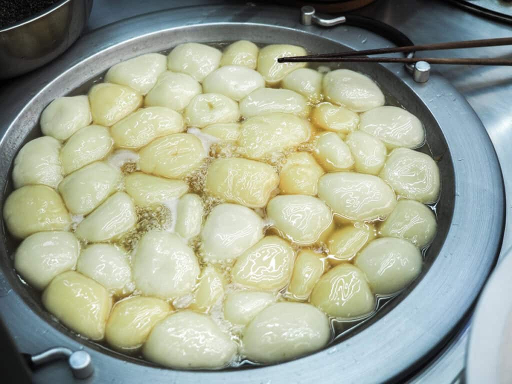 A round metal vat full of large balls of mochi boiling in water