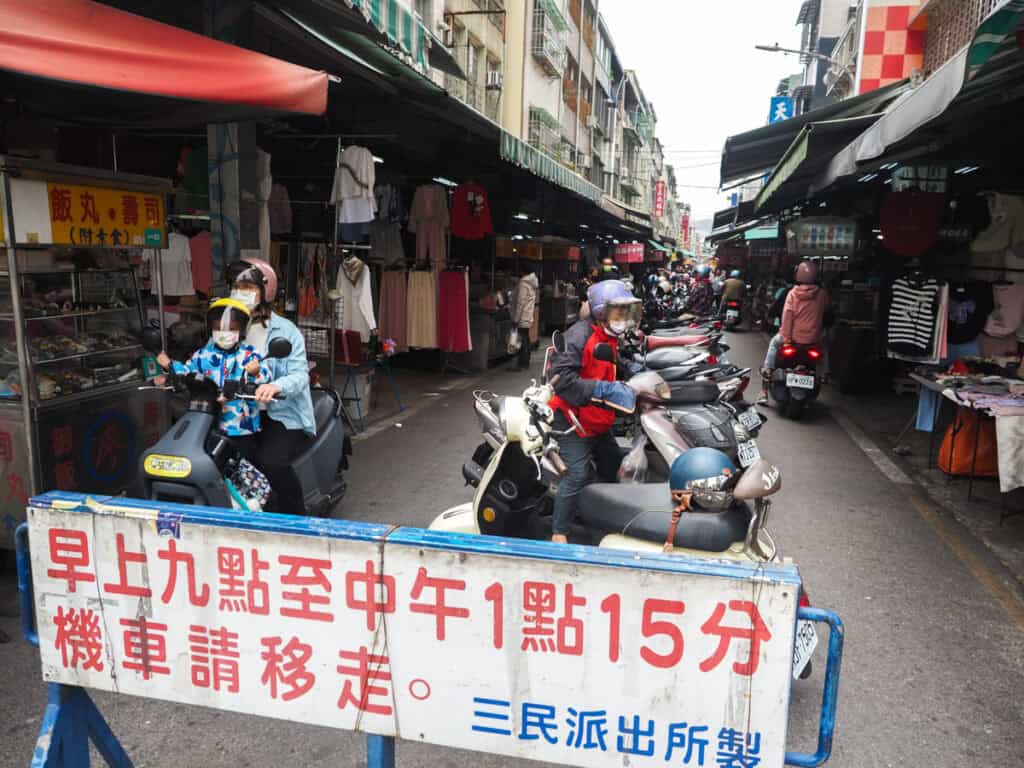 A barrier in front of Sanmin Street with scooters parked in the market street behind it