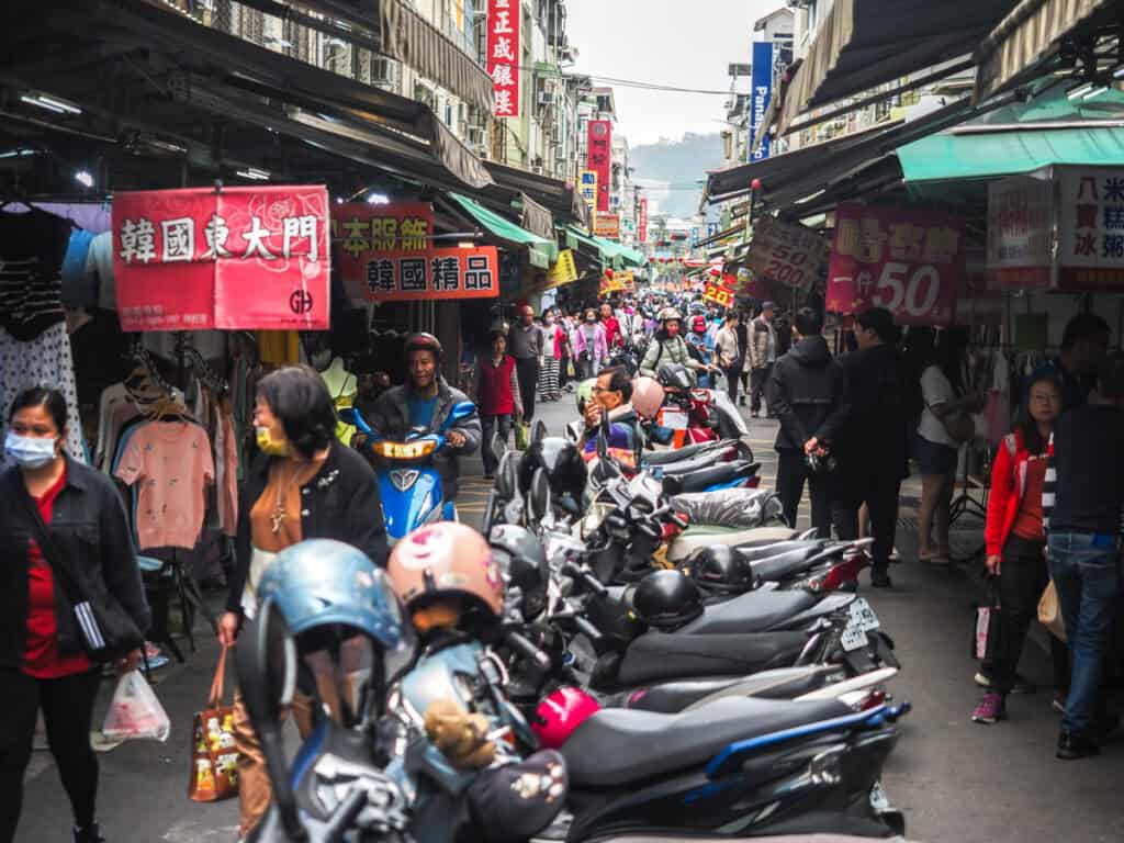 A row of parked scooters in narrow Sanmin Street and the entrance to the traditional market