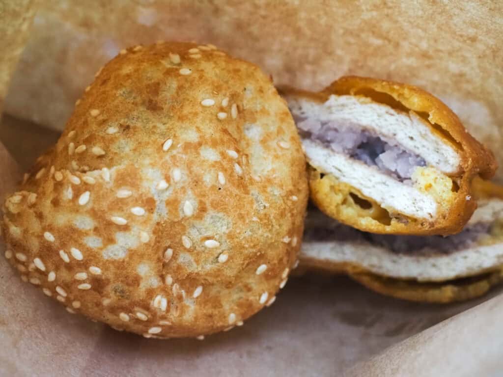 Close up of a deep fried sesame ball and taro cake inside a brown paper bag