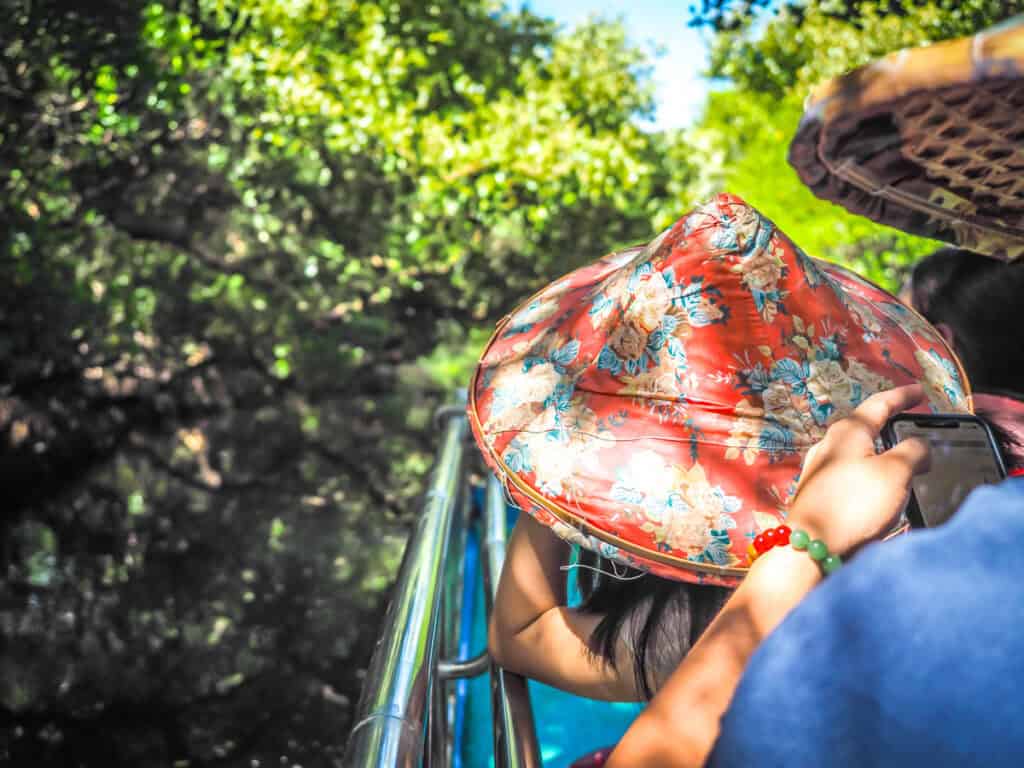 Some people in a boat with colorful farmers hats as it goes past trees in Sicao Green Tunnel