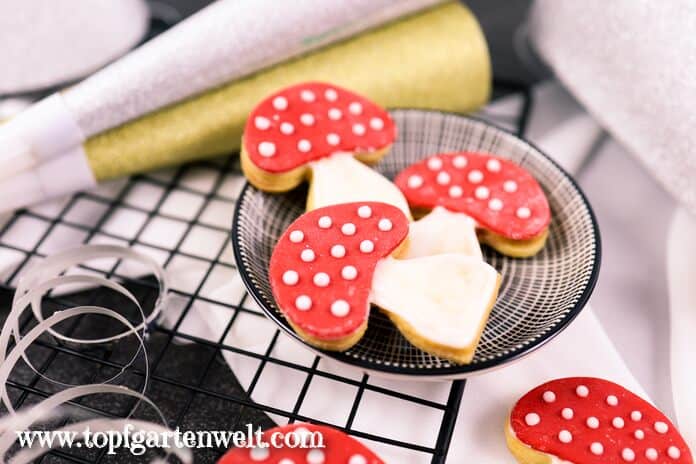Leckere Glücksbringer aus Mürbeteig in Form von Fliegenpilzen liegen in einer kleinen schwarzen Schale und warten darauf verschenkt zu werden.