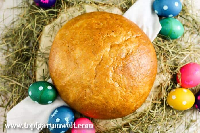 Ein Laib Osterbrot liegt auf einem Tuch. Darunter ist Heu. Daneben liegen gefärbte Ostereier.