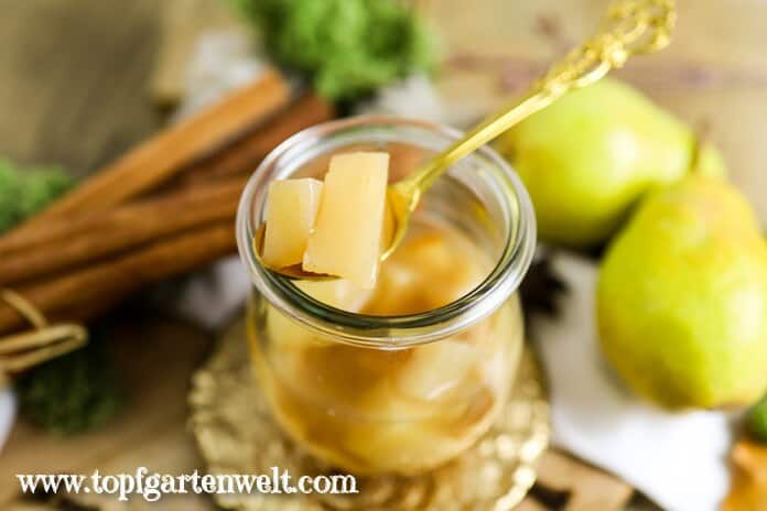 Ein leckeres Birnenkompott ist im Weckglas angerichet. Auf einem goldenen Löffel sind ein paar Birnenstücke zu sehen. Der Hintergrund ist herbstlich dekoriert und in ein warmes Licht getaucht.
