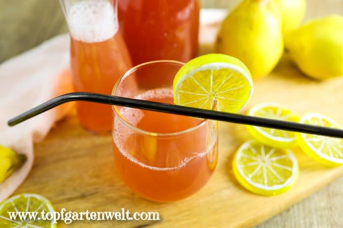 Ein Glas Quittensaft steht auf dem Tisch. Darüber liegt ein schwarzer Strohhalm. Daneben sind einige Zitronenscheiben zu sehen.