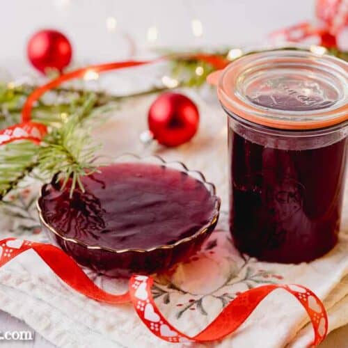Ein Weckglas gefüllt mit Glühweingelee steht neben einer ebenfalls damit gefüllten, kleinen Glasschale. Im Hintergrund ist ein Tannenzweig und rote Christbaumkugeln zu sehen.