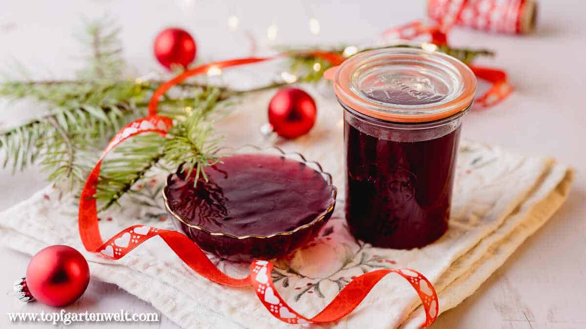 Ein Weckglas gefüllt mit Glühweingelee steht neben einer ebenfalls damit gefüllten, kleinen Glasschale. Im Hintergrund ist ein Tannenzweig und rote Christbaumkugeln zu sehen.