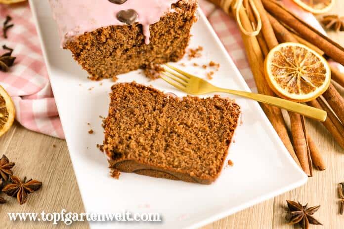 Ein Stück Glühweinkuchen liegt auf einer weißen Platte. Daneben sind getrocknete Orangen, Sternanis und Zimt zu sehen.
