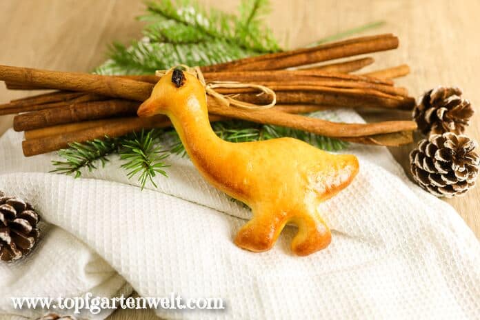 Eine Martinsgans aus Quark-Öl-Teig liegt auf einem weißen Tuch. Im Hintergrund sind Zimtstangen und ein Tannenzweig zu sehen.
