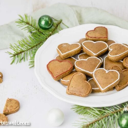 Diese sofort weichen Lebkuchen Plätzchen liegen auf einem weißen Teller. Im Hintergrund sind Tannenzweige und Weihnachtskugeln zu sehen.