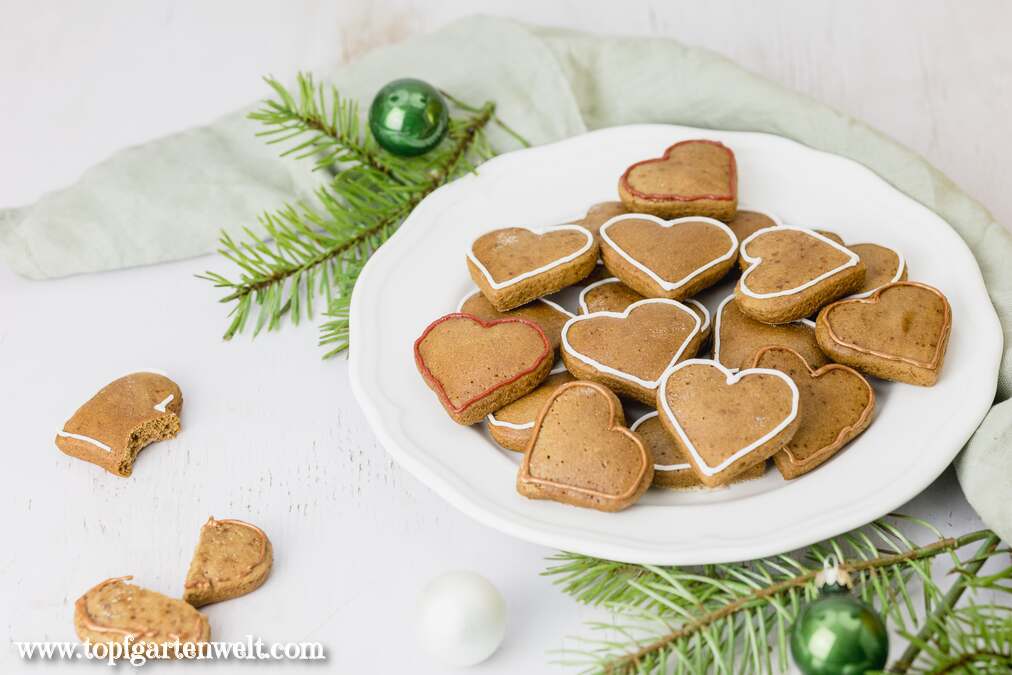 Diese sofort weichen Lebkuchen Plätzchen liegen auf einem weißen Teller. Im Hintergrund sind Tannenzweige und Weihnachtskugeln zu sehen.