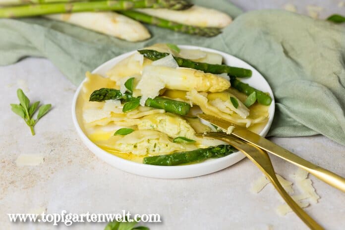 Selbst gemachte Spargel-Ravioli angerichtet auf einem weißen Teller. Darauf angelehnt ist goldenes Besteck. Im Hintergrund ist etwas Gemüse zu sehen.