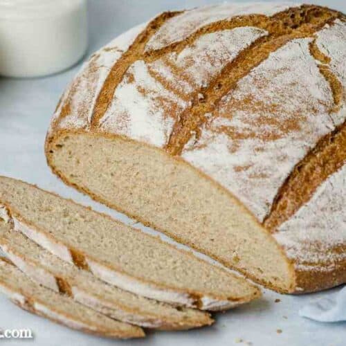 Das Dinkel Joghurt Brot ist angeschnitten und liegt auf einem hellblauen Tuch. Vor dem Brotlaib liegen drei Scheiben Brot.