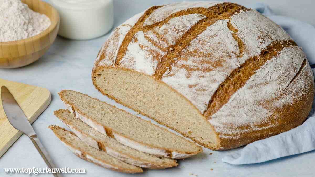 Das Dinkel Joghurt Brot ist angeschnitten und liegt auf einem hellblauen Tuch. Vor dem Brotlaib liegen drei Scheiben Brot.
