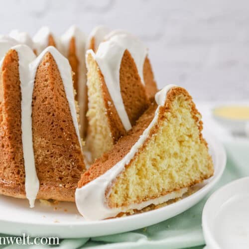 Ein einfacher Eierlikör Gugelhupf mit Öl steht auf einem weißen Teller. Als Untergrund dient eine grüne Tischdecke. Daneben ist ein kleines Teller, auf welchem zwei goldene Gabeln liegen. Der Kuchen ist angeschnitten.