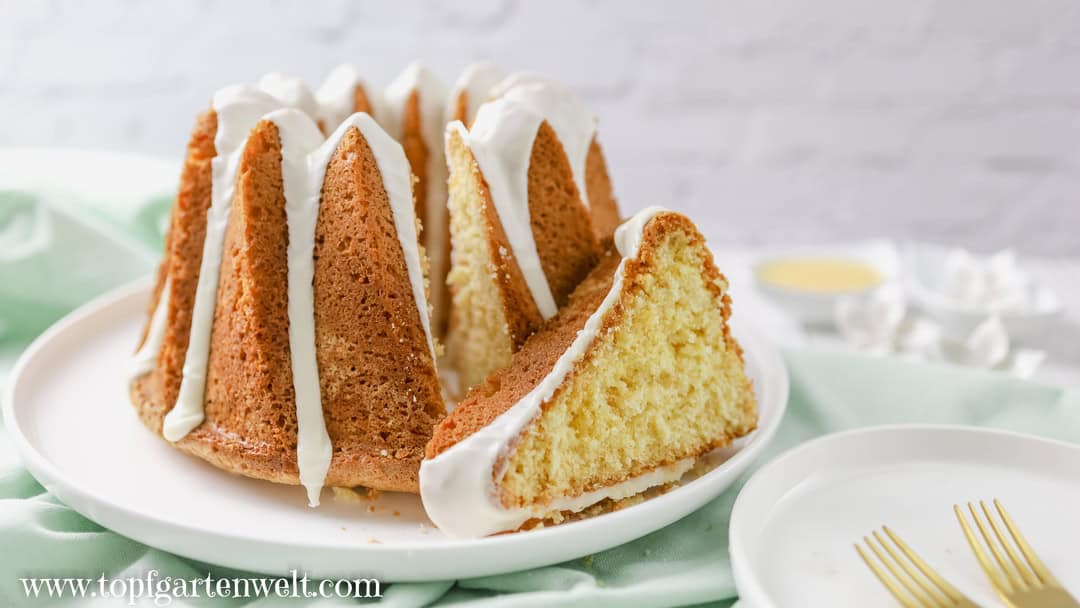 Ein einfacher Eierlikör Gugelhupf mit Öl steht auf einem weißen Teller. Als Untergrund dient eine grüne Tischdecke. Daneben ist ein kleines Teller, auf welchem zwei goldene Gabeln liegen. Der Kuchen ist angeschnitten.