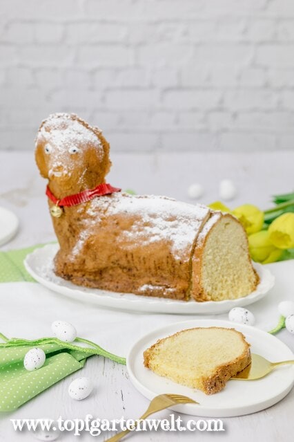 Ein österliches Motivgebäck in Form von einem Lamm steht auf einem weißen Teller. Es ist angeschnitten, so dass man das Innere gut sehen kann.