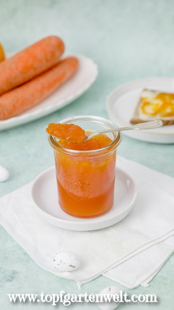 Auf einem Glas Ostermarmelade liegt ein silbener Löffel. Auf diesem ist ein wenig Fruchtaufstrich zu sehen. Im Hintergrund liegt eine Scheibe Brot.