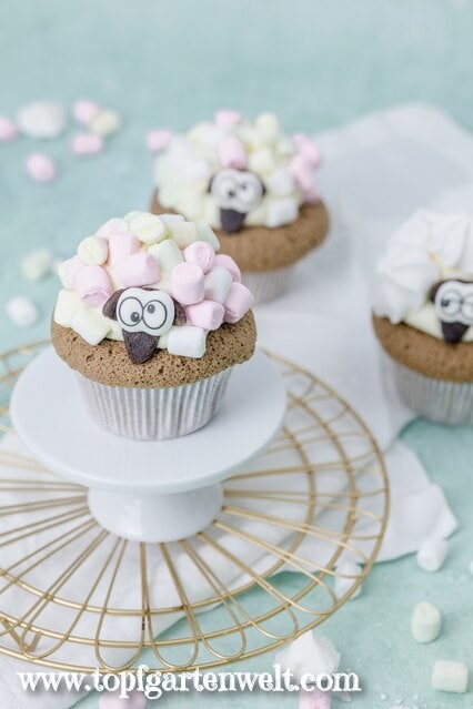 Oster Muffins, die aussehen wie ein Schaf. Eines steht auf einer kleinen Etagere. Im Hintergrund sind zwei weitere zu sehen.