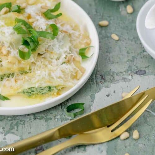 Ein Teller voll mit Bärlauch Ravioli garniert mit brauner Butter, Parmesan und Pinienkernen. Im Vordergrund liegt goldenes Essbesteck.
