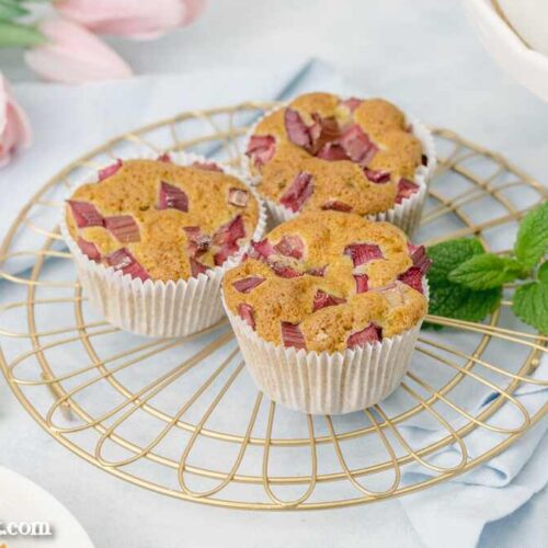 Köstliche Rhabarber-Muffins mit Buttermilch und einem Hauch Zitronenmelisse. Sie stehen auf einem goldenen Abkühlgitter.