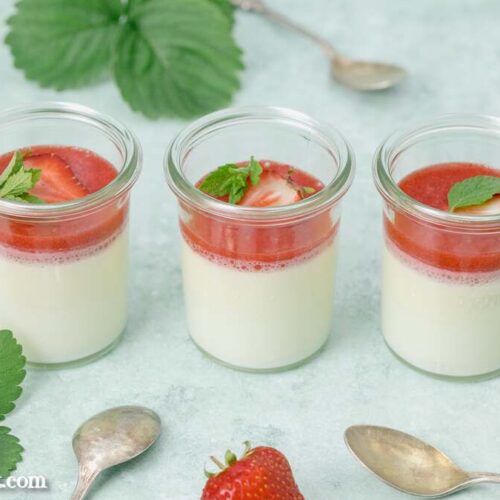Drei Gläser Panna Cotta mit einem Fruchtspiegel aus Erdbeeren warten darauf vernascht zu werden. Die Löffel liegen schon bereit.