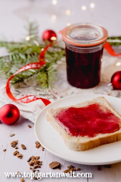 Das selbst gemachte Glühweingelee wurde auf eine Scheibe Toastbrot gestrichen. Im Hintergrund ist ein noch volles Marmeladenglas als auch ein Tannenzweig und rote Christbaumkugeln zu sehen.