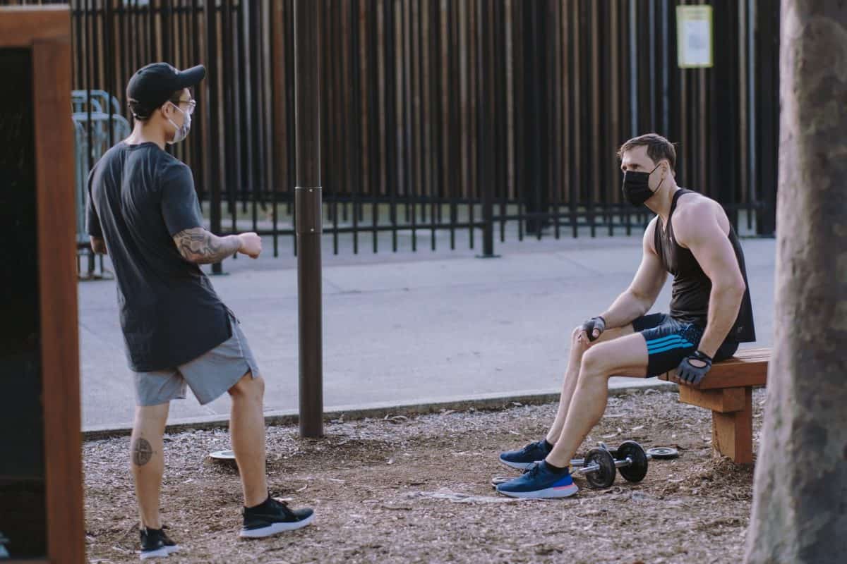 Two guys in the park with masks on and practicing social distancing.