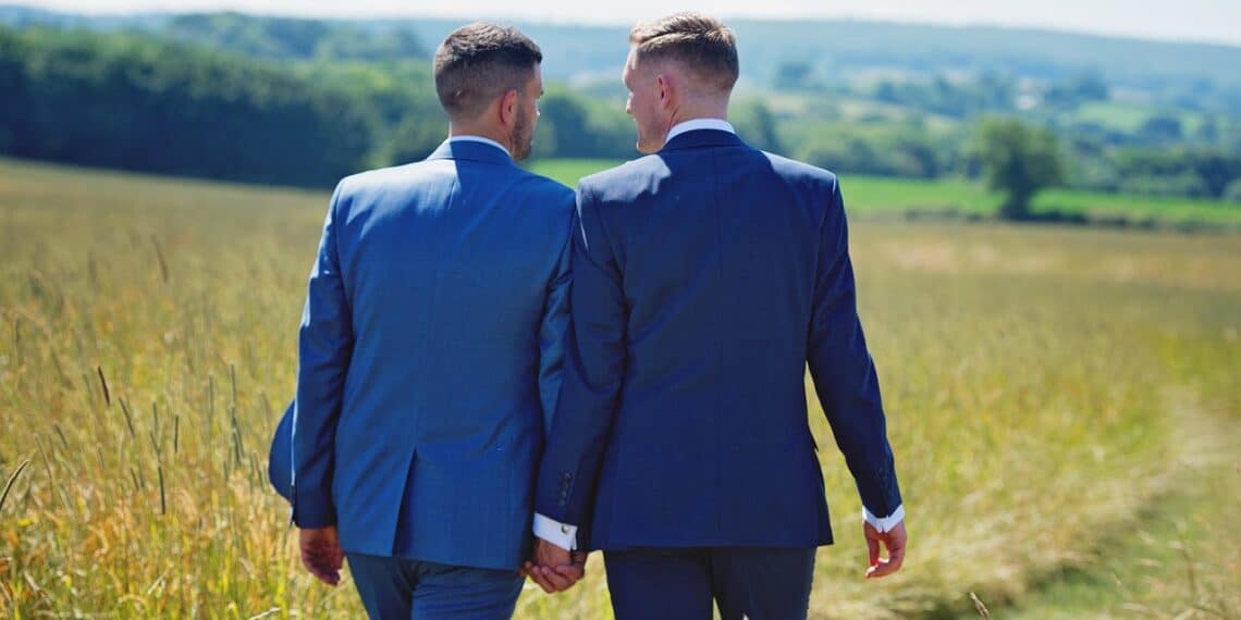 Same-sex marriage a male couple walks through a field holding hands