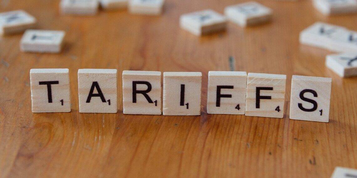 Scrabble tiles standing upright on a wooden table to spell tariffs