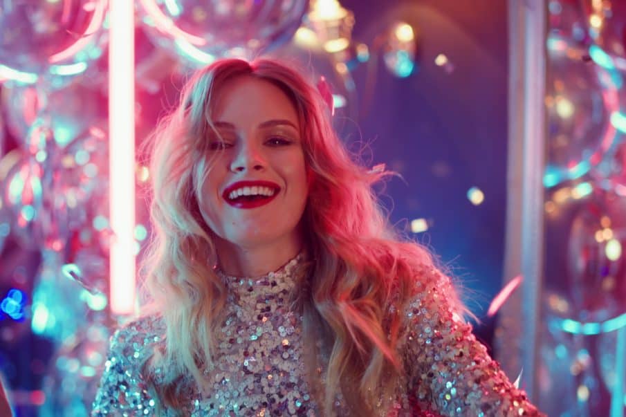 A party photographer capturing a joyful portrait of a woman in a sparkling sequin dress under vibrant club lighting.