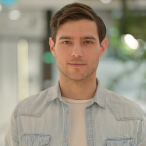 Professional male portrait for dating apps taken in a studio; a man in a light denim shirt against a softly blurred office background.