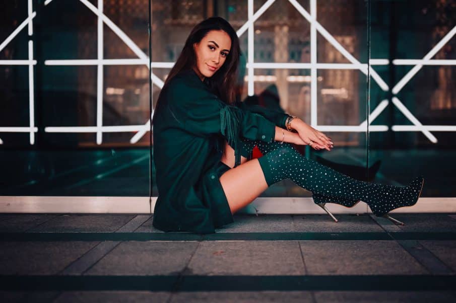 Stylowa modelka w kozakach na tle podświetlonej fasady budynku. Fotografia kobieca warszawa – sesja fashion nocą.