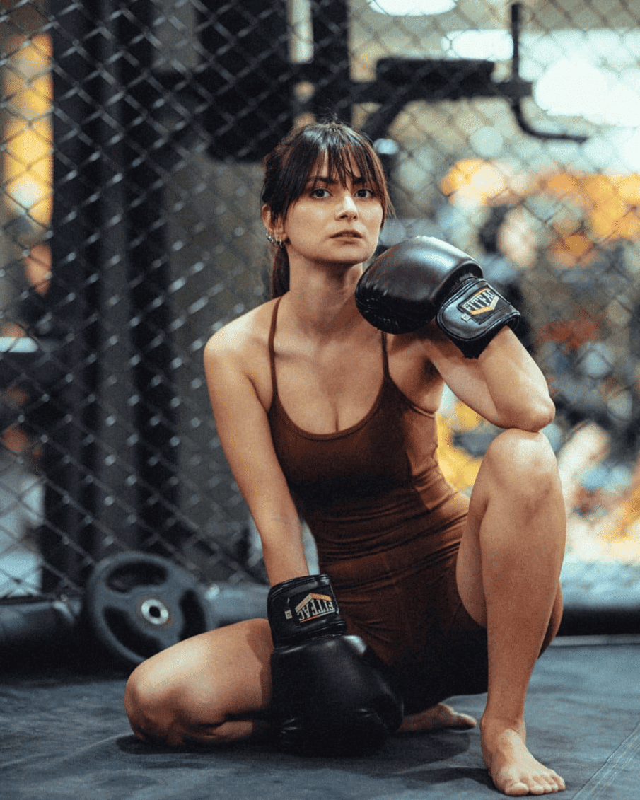 Portret kobiety w bokserskich rękawicach w klatce na siłowni. Profesjonalne zdjęcia portretowe w klimacie sportowym