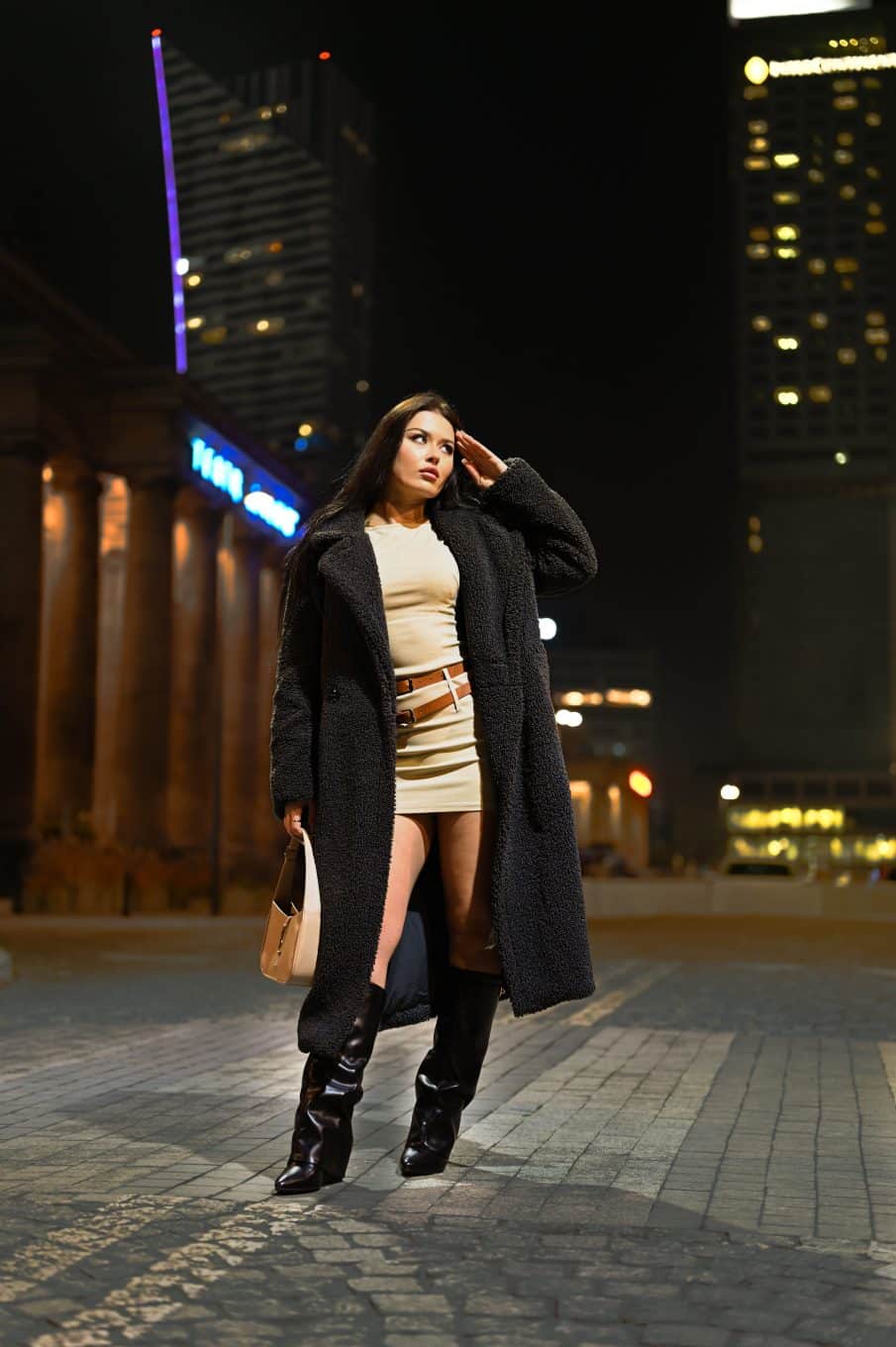 Kobieta w futrzanym płaszczu i torebką na tle nocnych świateł. Fotografia kobieca warszawa – sesja wizerunkowa