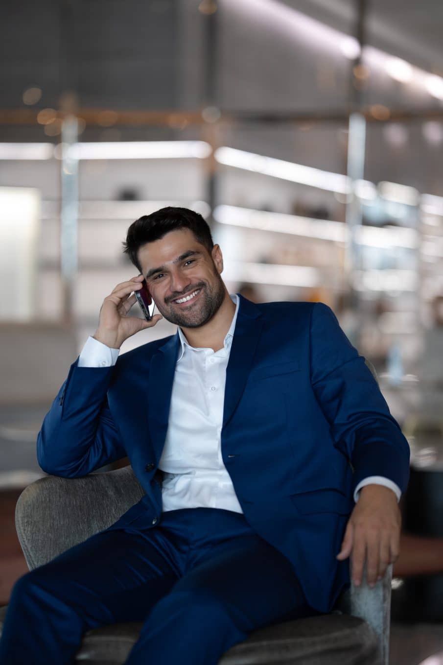Profesjonalny portret biznesowy uśmiechniętego mężczyzny w granatowym garniturze, rozmawiającego przez telefon. Zdjęcie wykonane w nowoczesnym biurze przez fotografa z warszawy. Idealny przykład portretu korporacyjnego.