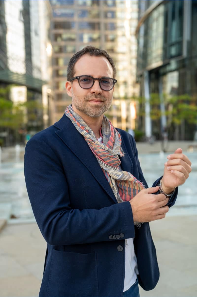 Biznesowy portret mężczyzny w marynarce i okularach na tle nowoczesnych biurowców. Profesjonalne zdjęcia korporacyjne