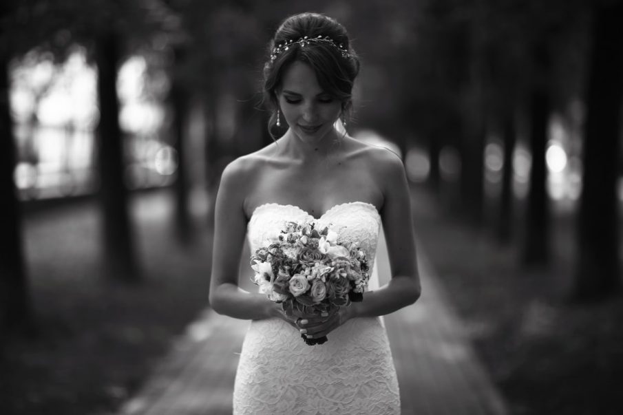 Nastrojowa fotografia slubna: czarno-biały portret panny młodej z bukietem w parku. Intymny reprtaż ślubny.