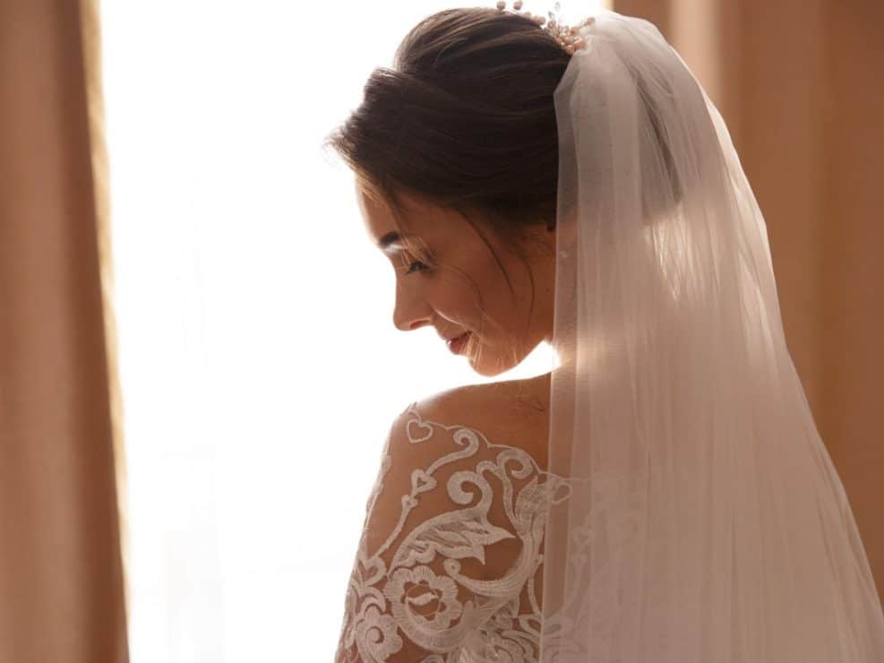 Subtelny portret panny młodej z welonem, ukazujący koronkę sukni. Artystyczna fotografia ślubna