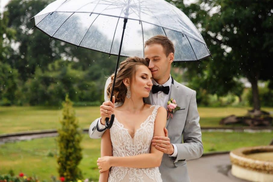 Para młoda pod przezroczystą parasolką w deszczu. Profesjonalna fotografia slubna w plenerze.