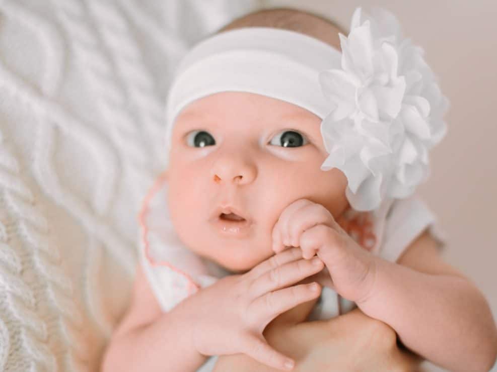 Reportaż chrzest warszawa: urocze zdjecia niemowlęcia z białą opaską i kwiatkiem, wykonane przez fotograf na chrzciny.