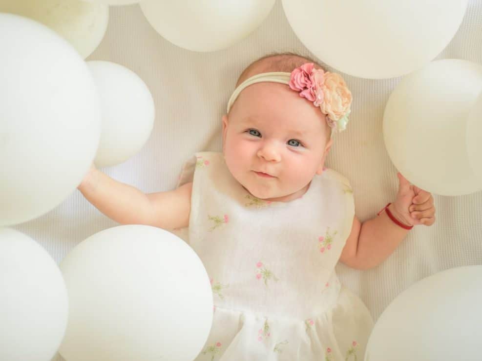 Fotograf chrzest warszawa: uroczy portret niemowlęcia otoczonego białymi balonami. Pomysł na dekoracje i sesję podczas przyjęcia chrzcielnego w warszawie.