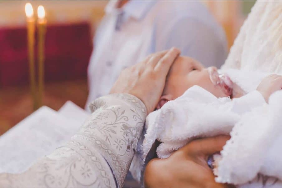 Fotograf chrzest warszawa cena: delikatne ujęcie z ceremonii w kościele. Kapłan błogosławi niemowlę, ubrane w białą szatkę. Kadr pełen czułości i nastroju.