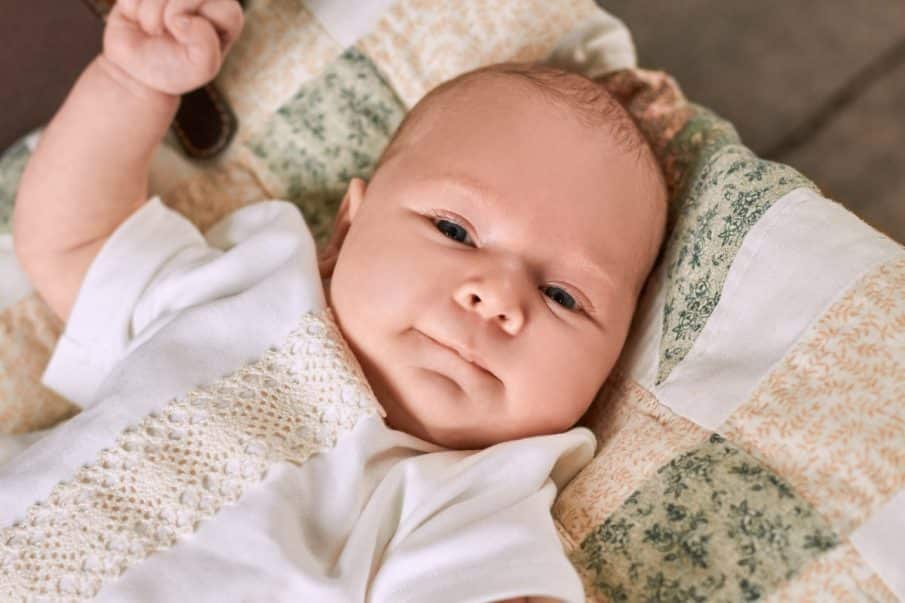 Fotograf chrzest warszawa: delikatny portret dziecka w szacie do chrztu. Zbliżenie na twarz niemowlaka, pamiątka z reportażu chrzcin.